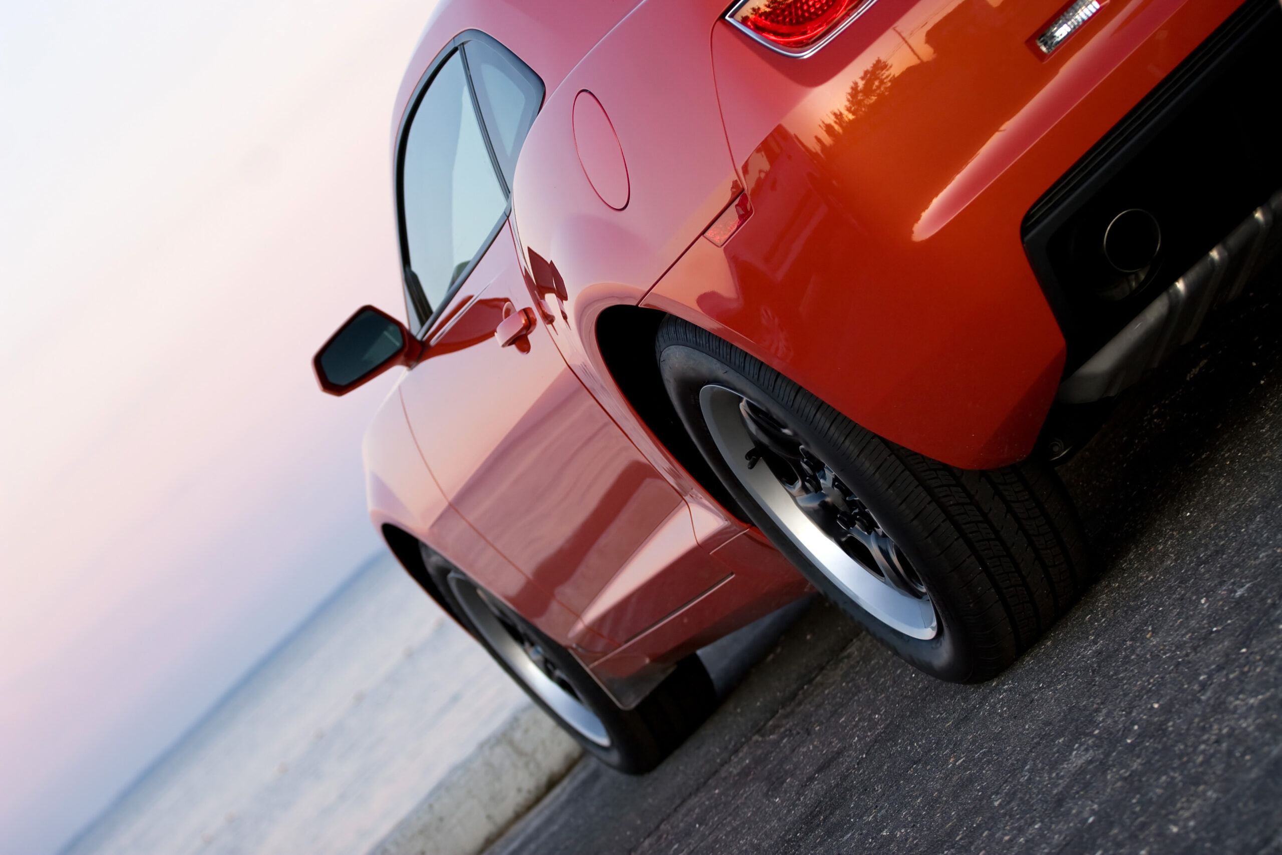 A modern sports car parked at the beach around sunset.