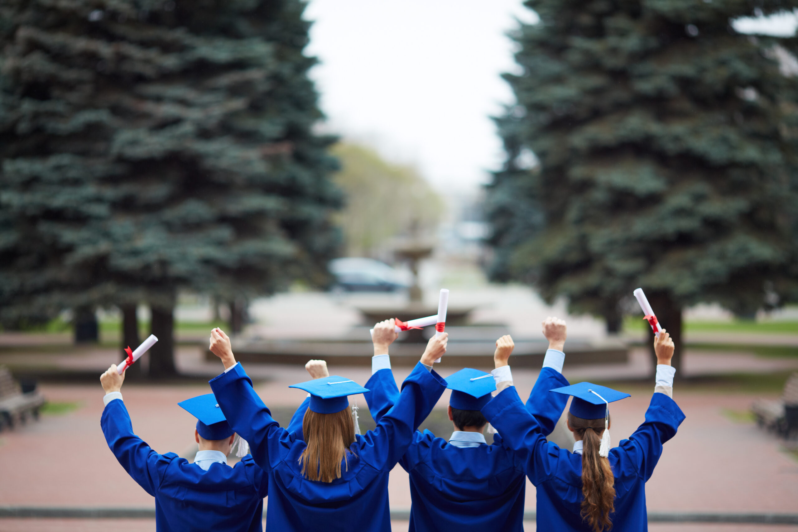 Backs of ecstatic students in graduation gowns holding diplomas