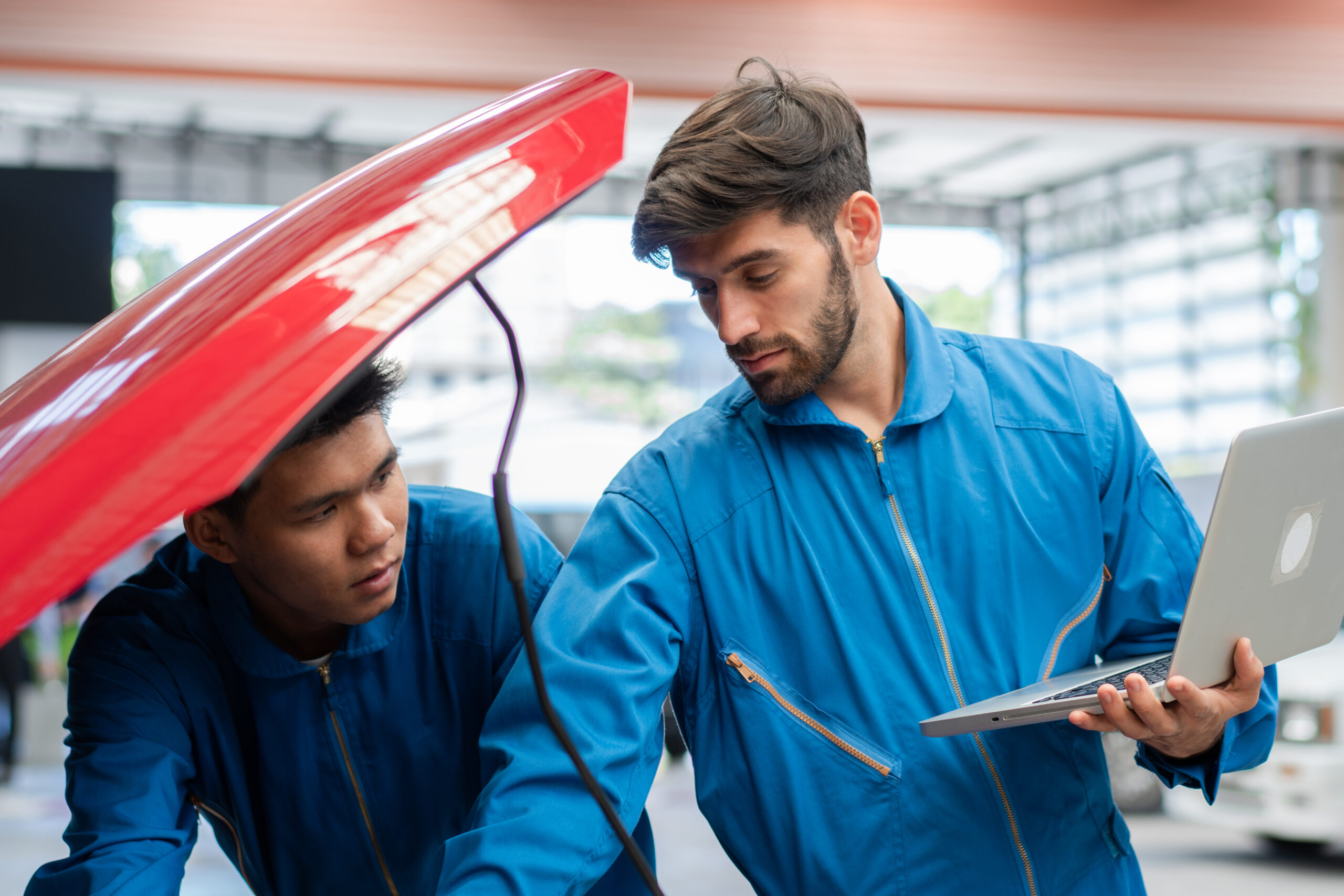 Caucasian automobile mechanic man using laptop computer diagnostic and repairing car while his colleague checking in radiator bonnet at garage automotive, motor technician maintenance after service