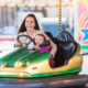 Cute little girl with her mother having fun at fun fair, driving a bumper car, amusement park