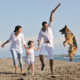 happy young family in white clothing have fun and play with beautiful dog at vacations on beautiful beach