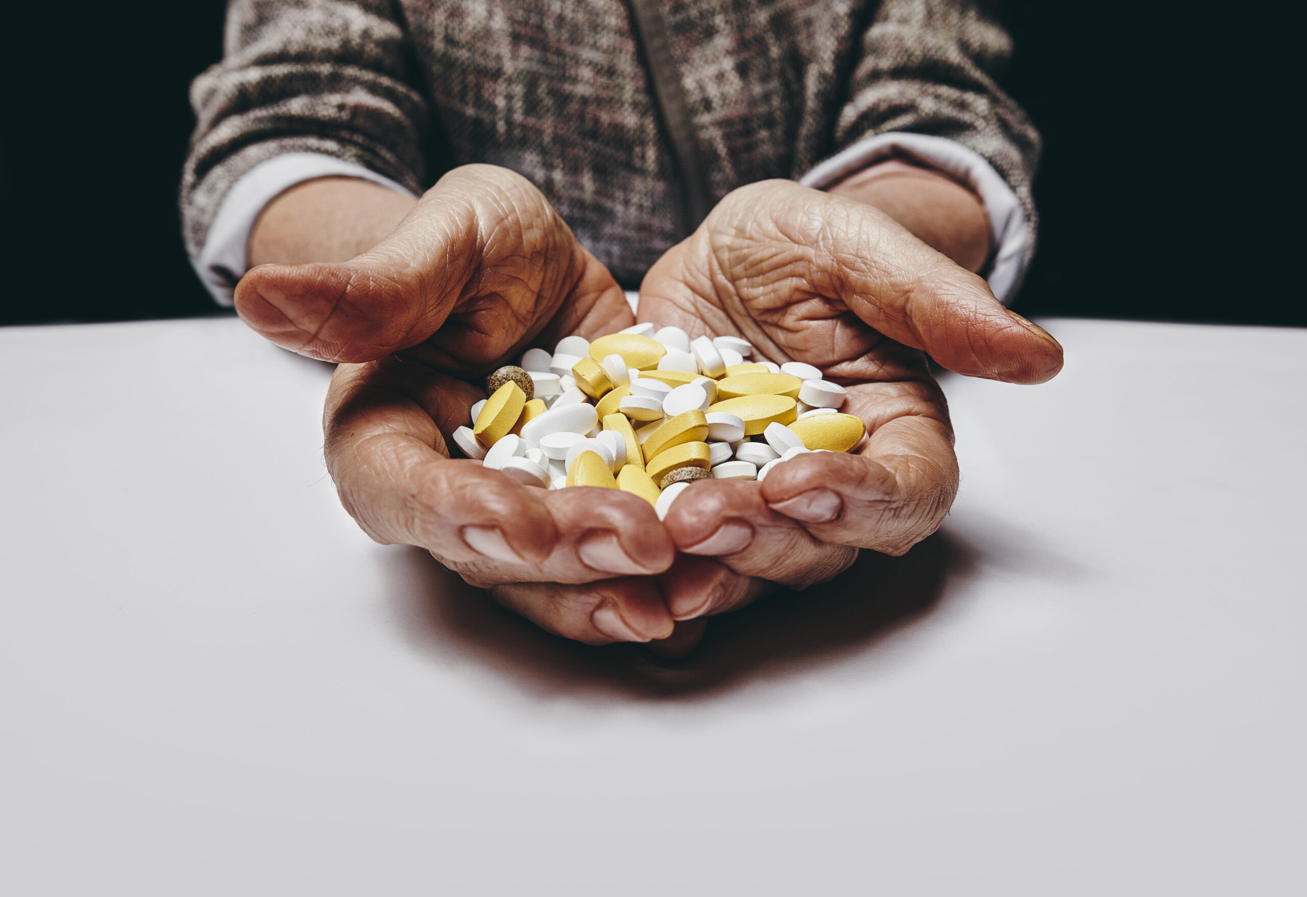 Old woman holding pills and medicine while sitting at a table. Focus on hands and pills. Close-up shot of senior female hands holding pills.