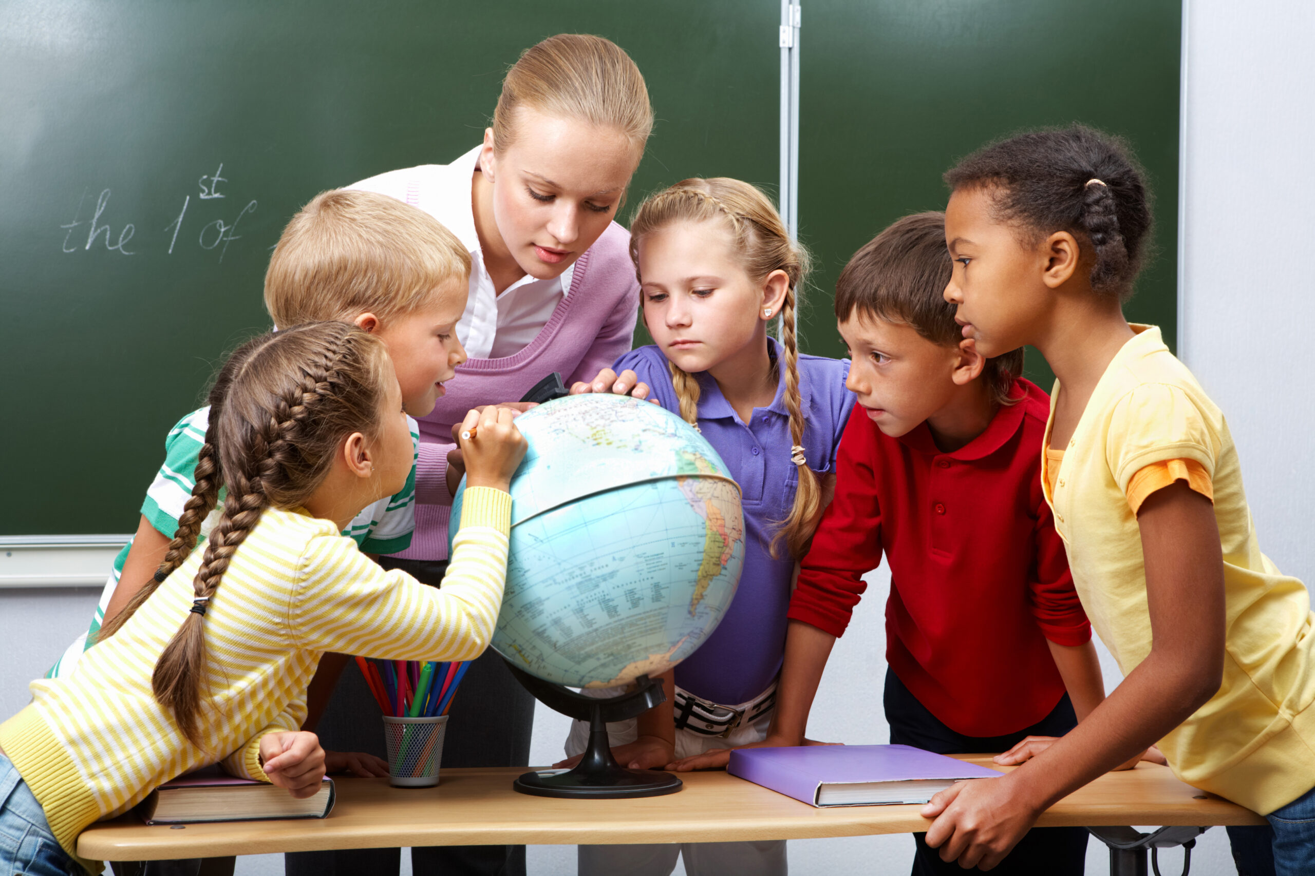 Portrait of pupils looking at globe while listening to teacher during geography lesson