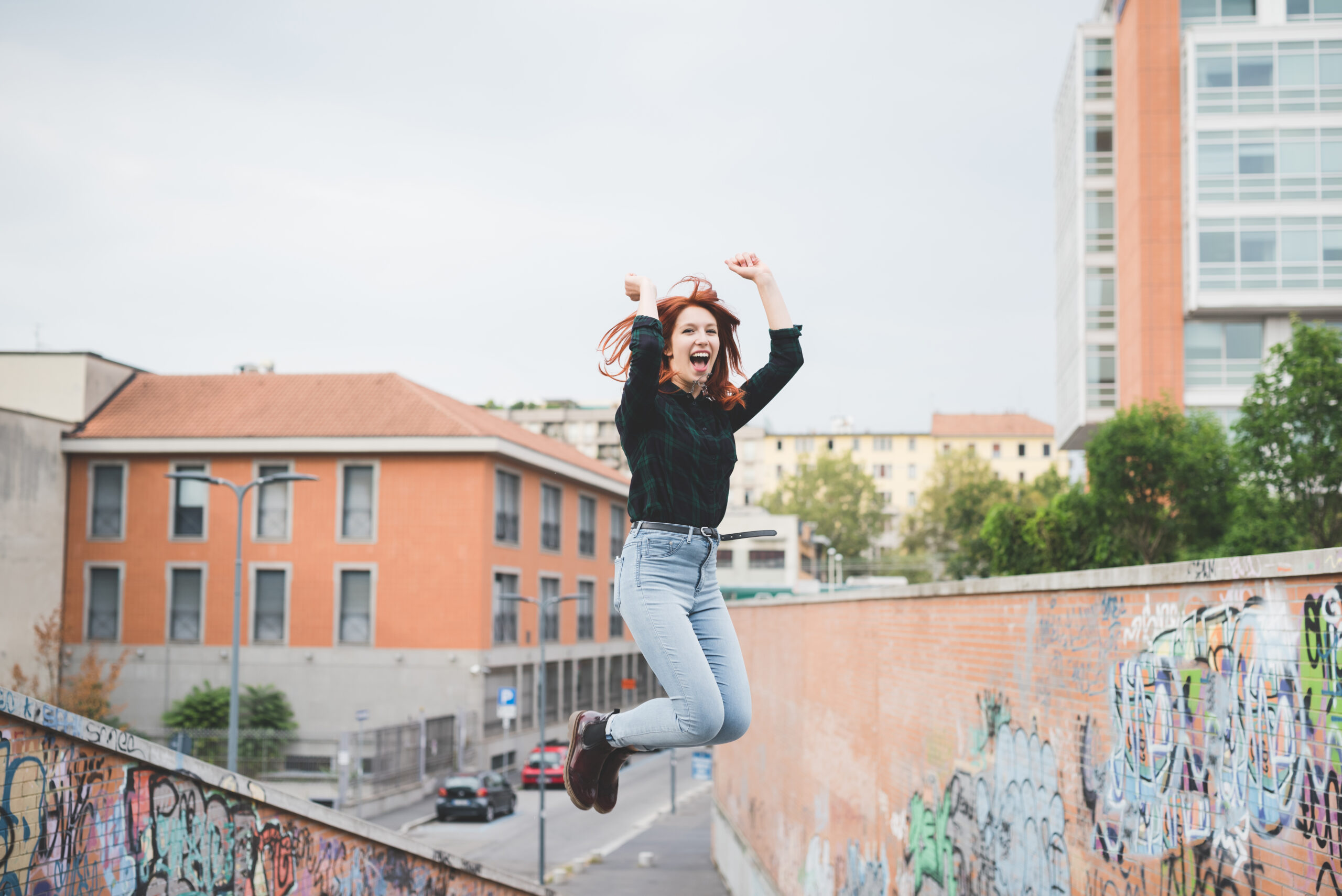 Young handsome caucasian redhead straight hair woman jumping outdoor in the city, hands up, laughing - girl power, goal, success concept