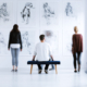 Man sitting on stool and looking at drawings while spending time in art center with other visitors