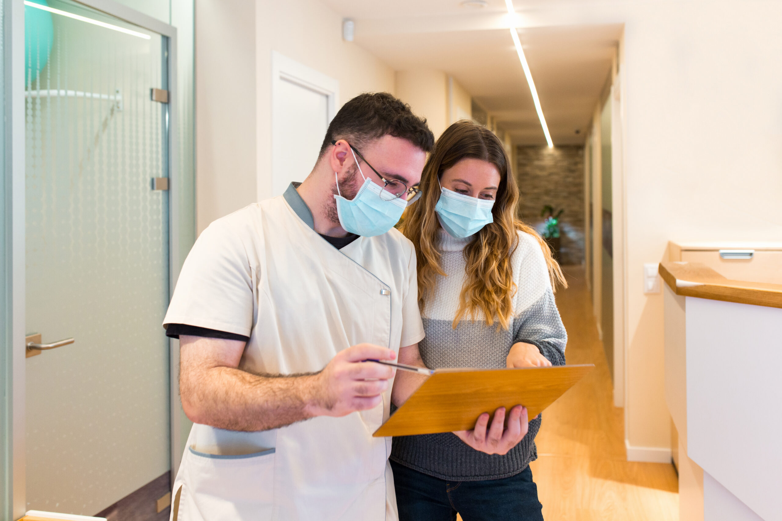 Front view of a nurse explaining notes to female patient in health center both wearing a surgical face mask.