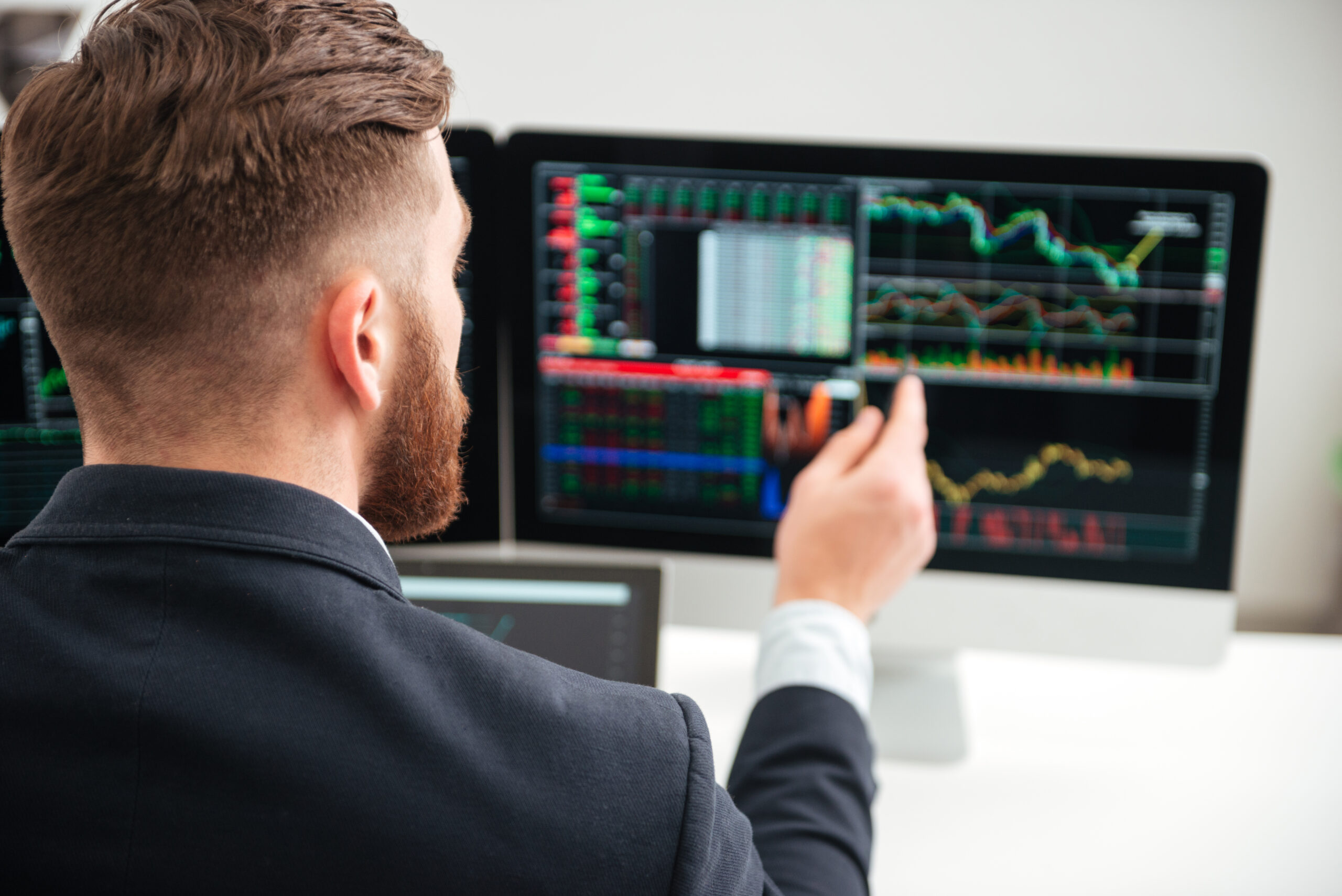 Back view of bearded young businessman woking with graph and charts on computer