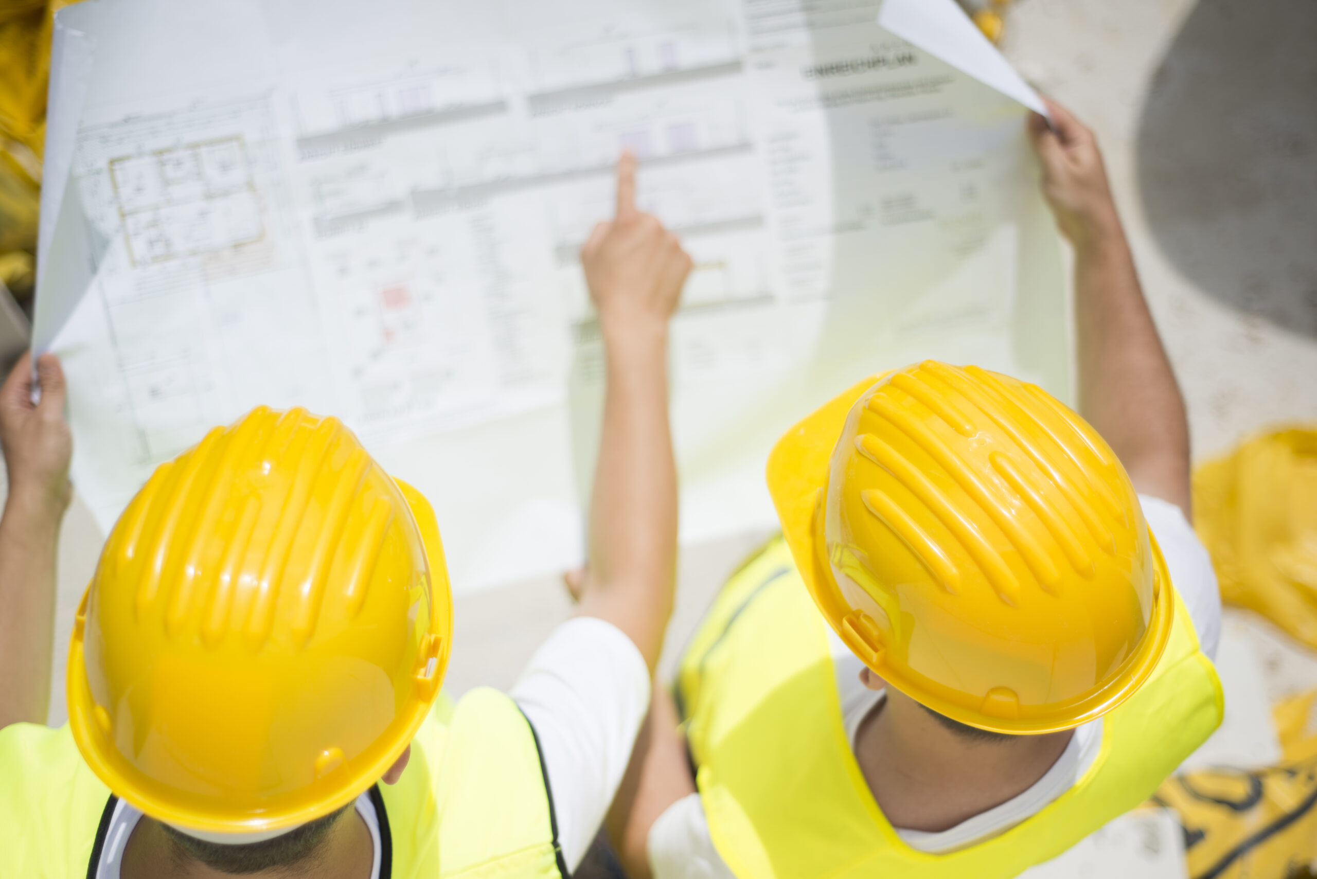 Engineer builders in safety vest with blueprint at construction site