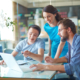 Group of three successful business partners in casual discussing data in laptop at meeting in office