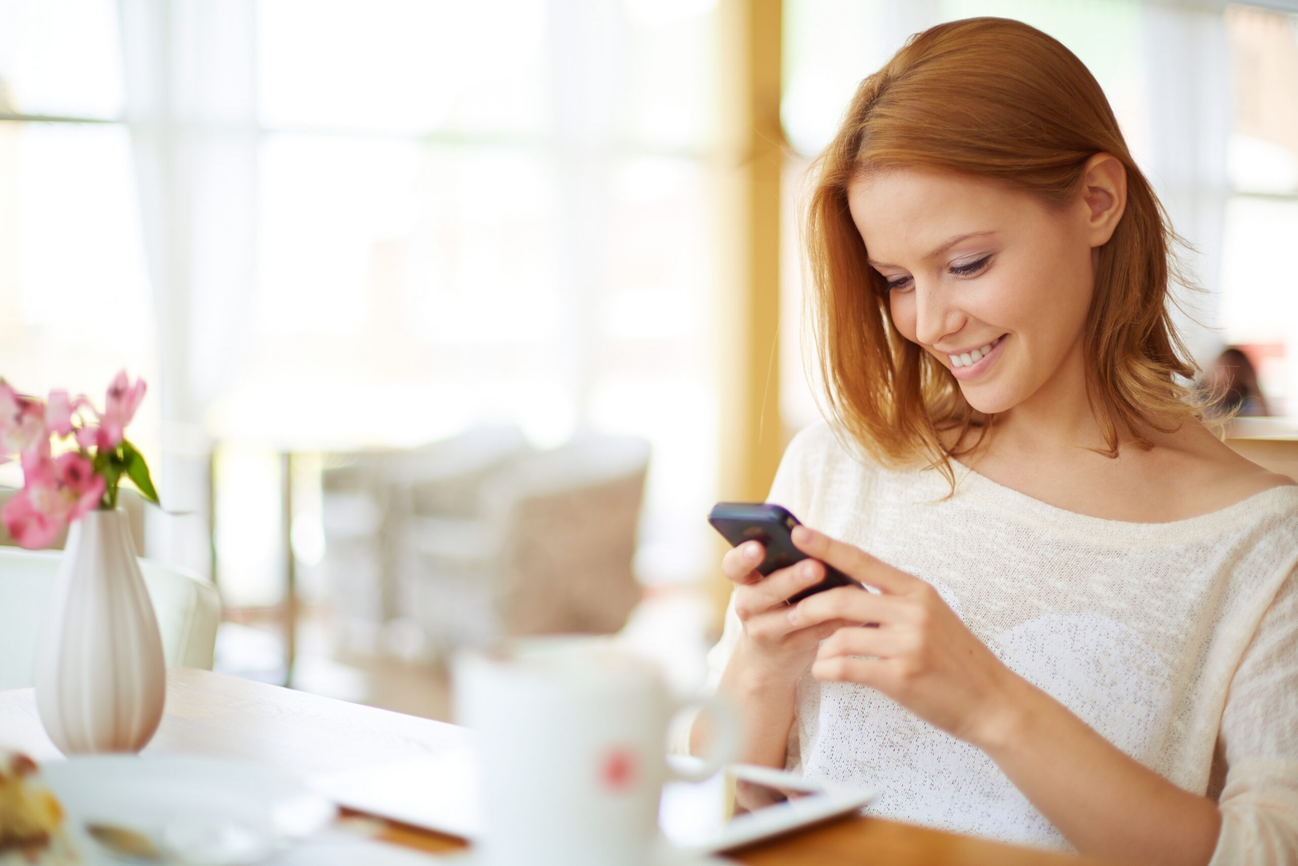 Image of young female reading sms on the phone in cafe