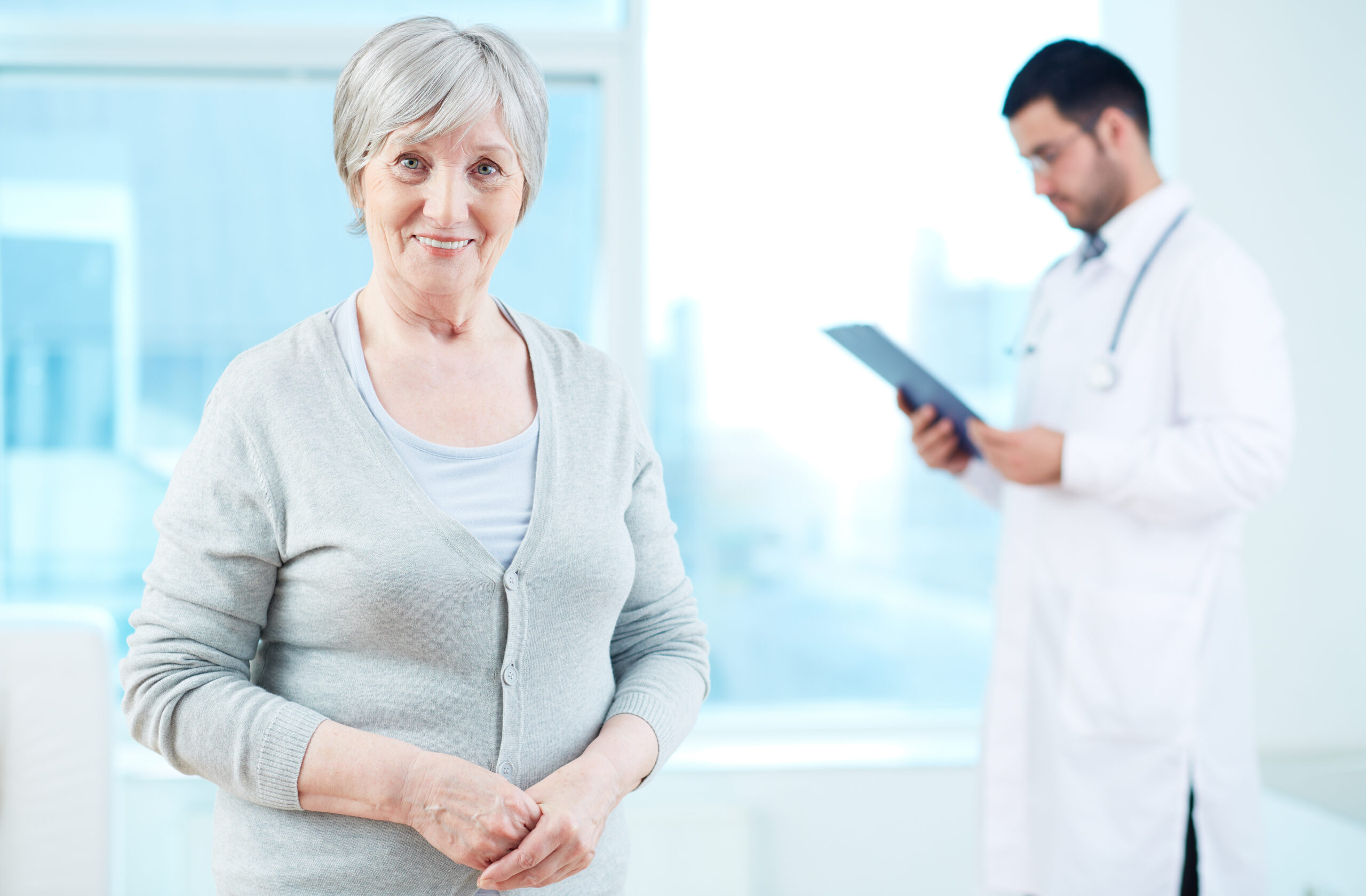 Senior patient looking at camera with doctor working on background