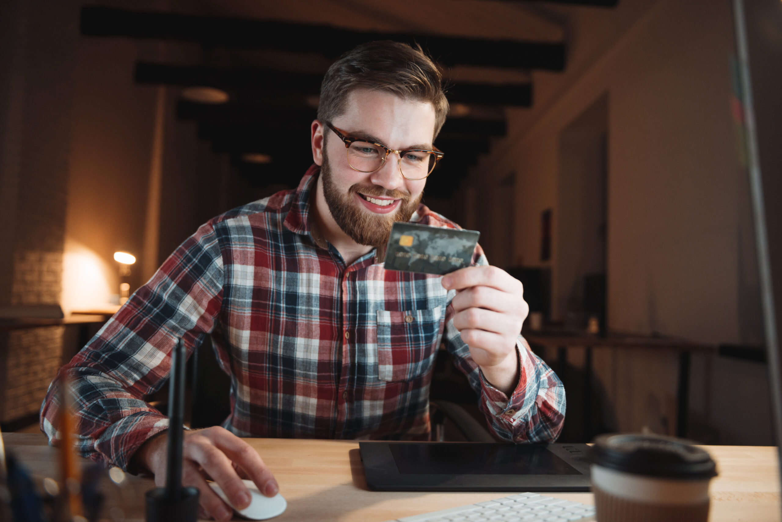 Smiling casual business man paying online with his credit card at office