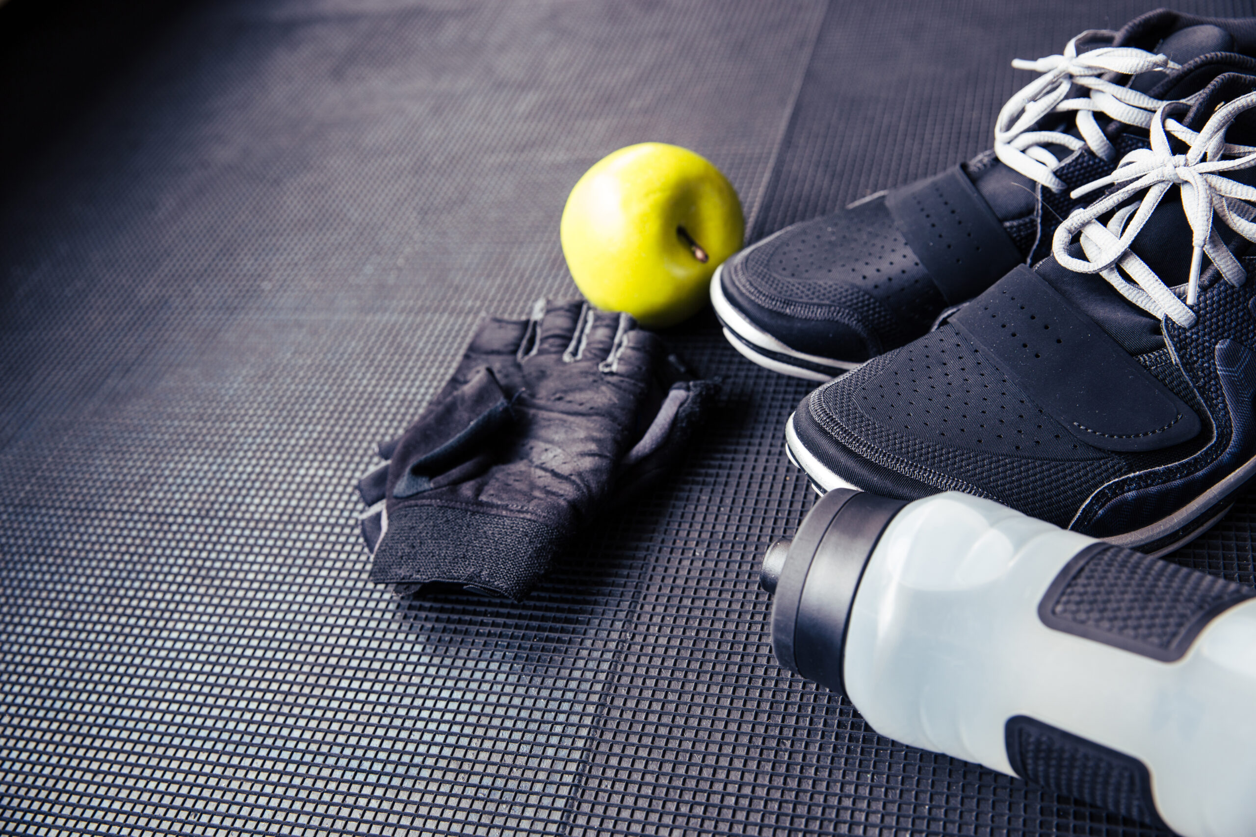 Closeup image of a sports gloves, sneakers, bottle with water and green apple on rubber floor