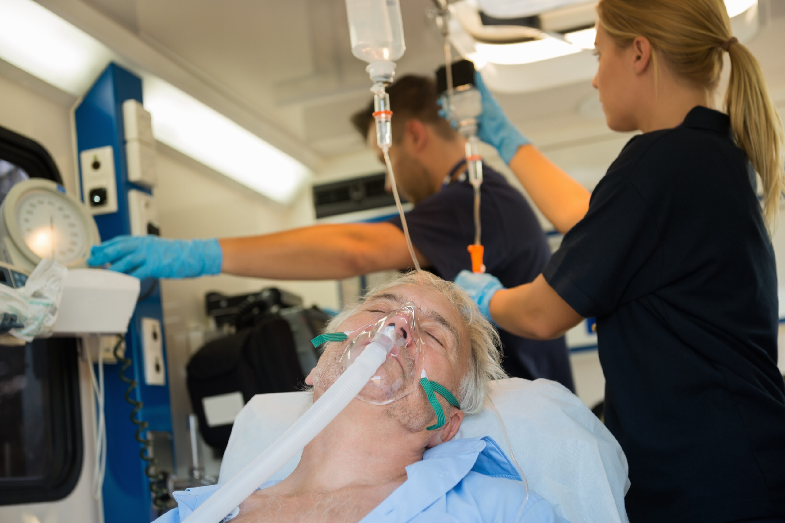 Unconscious senior patient with oxygen mask in ambulance car