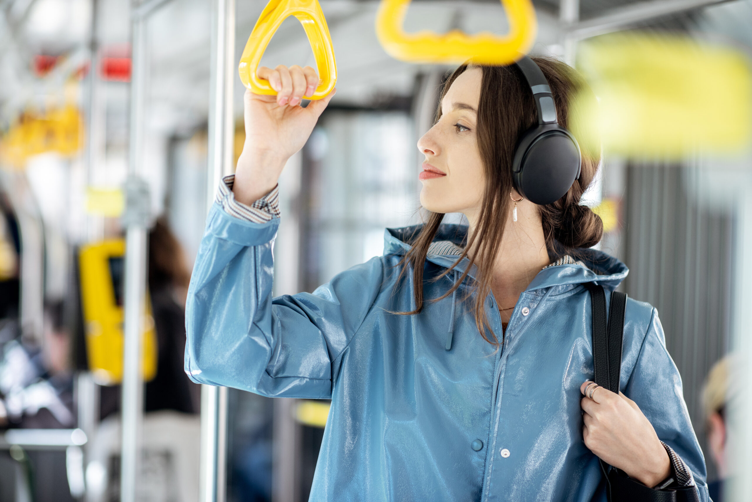 Young stylish woman enjoying trip in the public transport, standing with headphone while moving in the modern tram