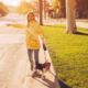 Full length young female with funny Beagle on leash stretching out arm and catching taxi while standing on roadside near park in city